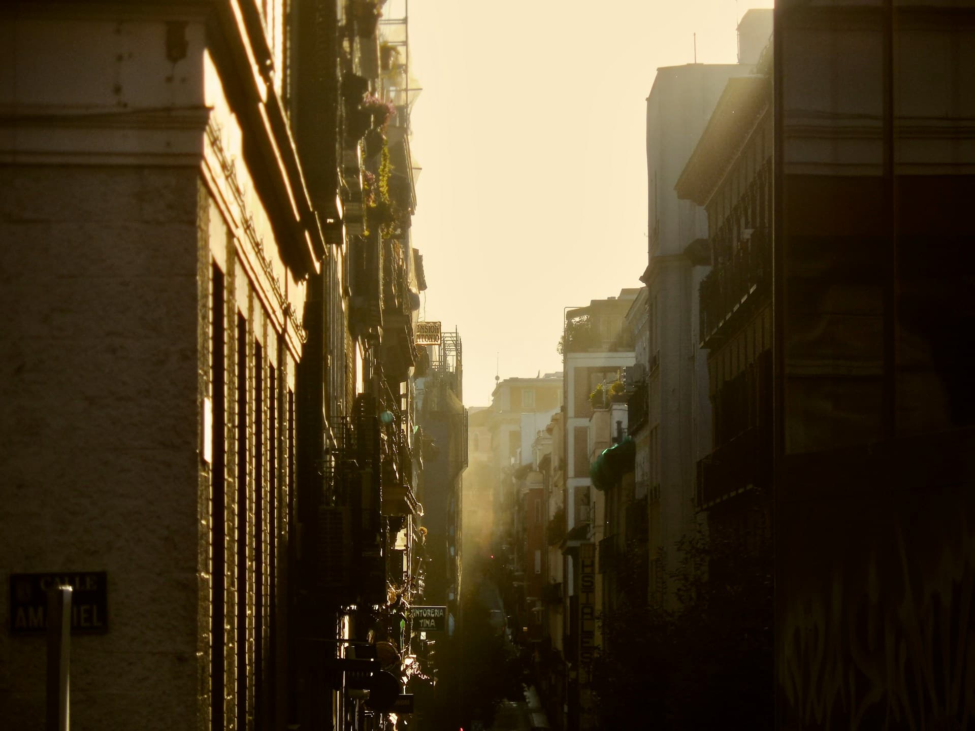Sunlight streaming down a narrow street in Malasaña with traditional balconies.