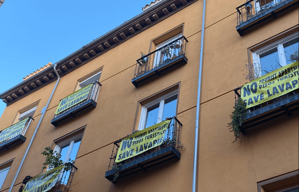 Yellow banners protesting short-term tourist apartments hanging from the balconies of a traditional residential building in Madrid Centro.